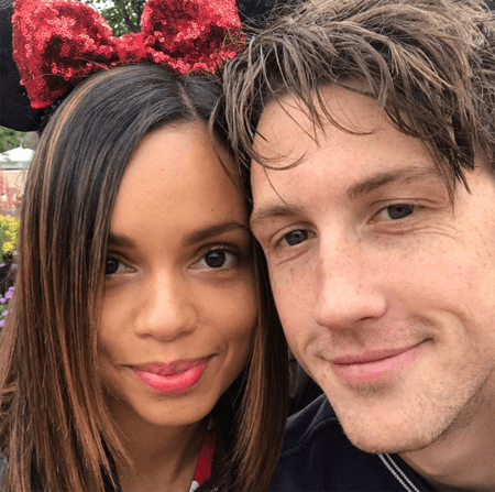 Georgina Campbell posing alongside Dawson Taylor wearing a red minnie mouse bow. The couple smiles together.